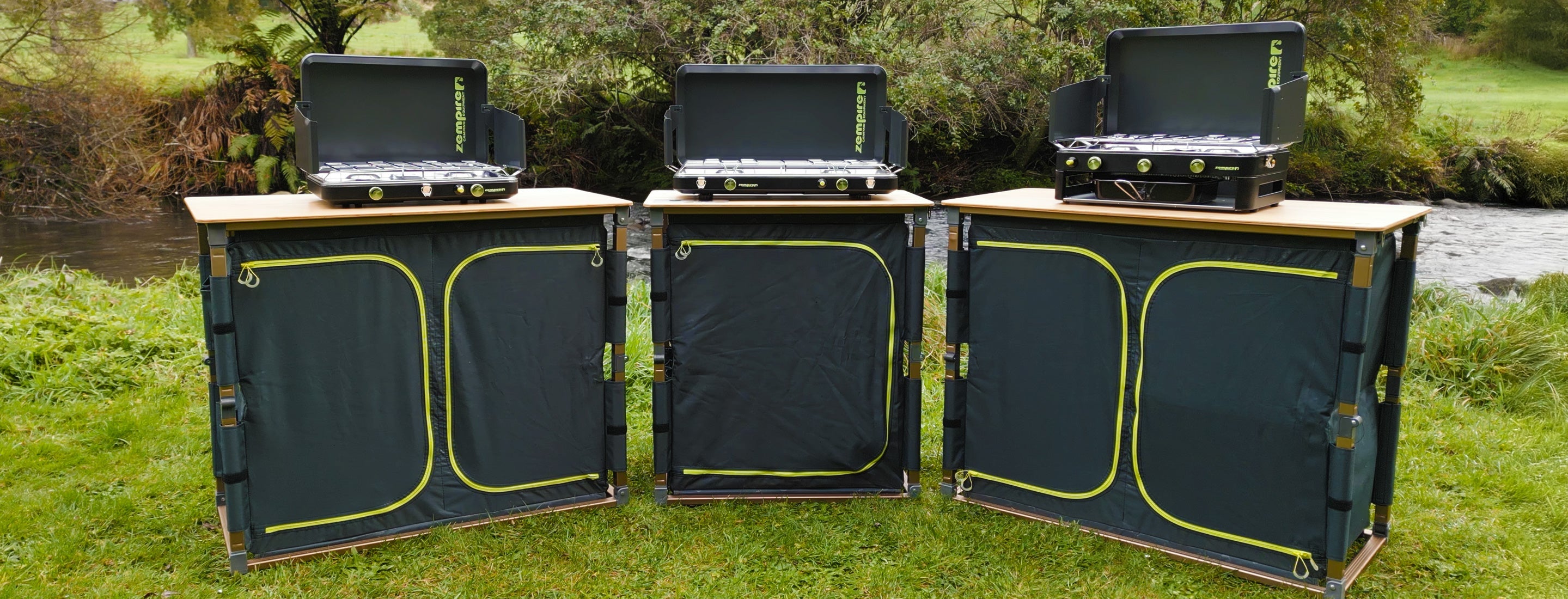 Three portable outdoor kitchen units with stoves on a grassy area.